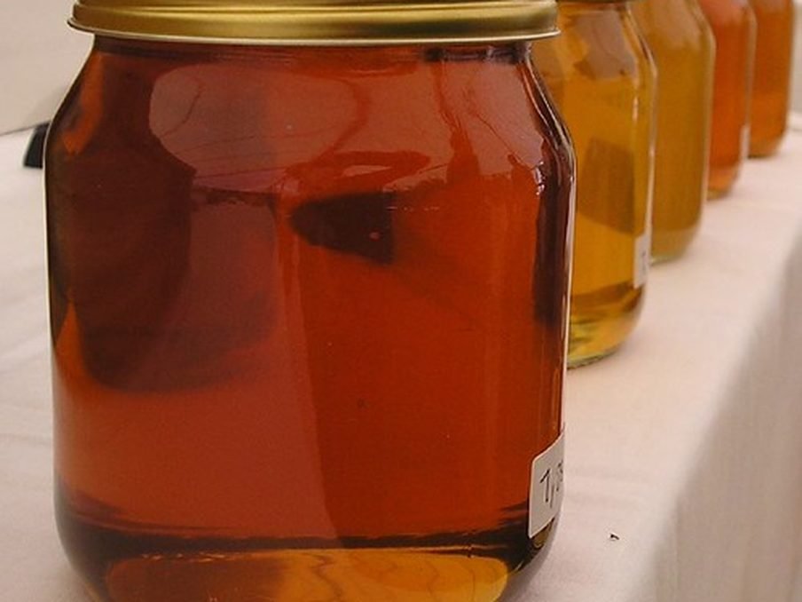 A glass jar of golden honey with a dipper